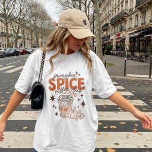 White t-shirt with "Pumpkin Spice Coffee Club" text and autumnal graphics on a street.
