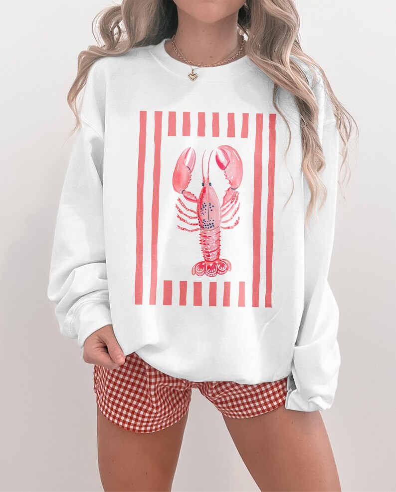 White crewneck sweatshirt with watercolor lobster graphic and red stripes.