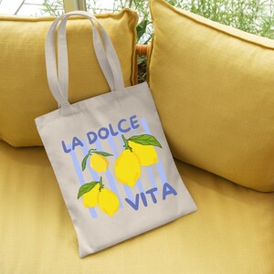 A white tote bag with a printed design of lemons and the text "LA Dolce Vita" is placed on a yellow couch.