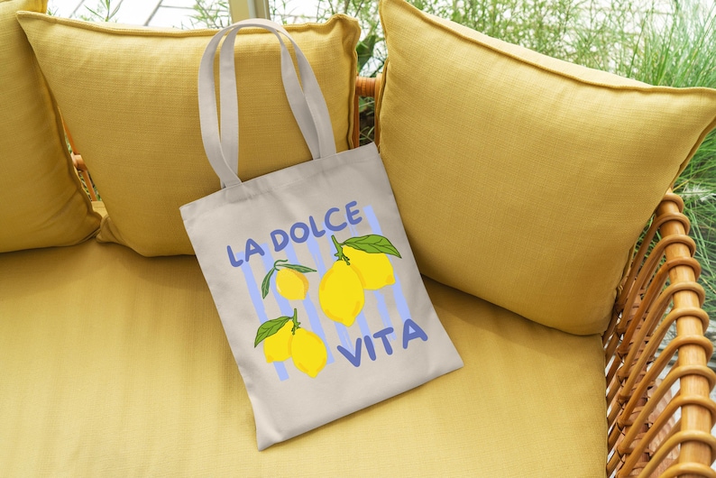 A white tote bag with a printed design of lemons and the text "LA Dolce Vita" is placed on a yellow couch.