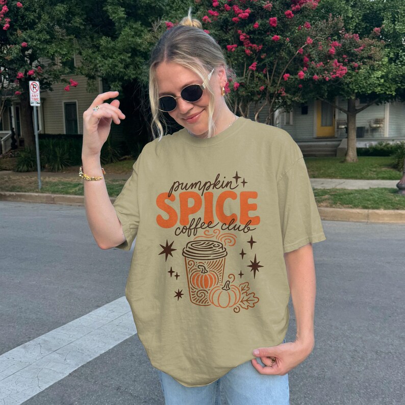 Light tan t-shirt with pumpkin spice coffee club graphic and pumpkins.