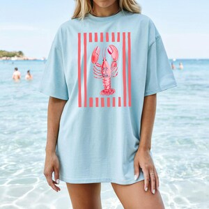 Light blue t-shirt with coral lobster and red striped graphic on chest.