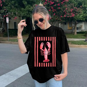 Black t-shirt with a pink lobster graphic and vertical stripes.