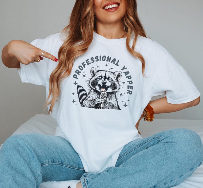a woman sitting on a bed with a raccoon t - shirt on