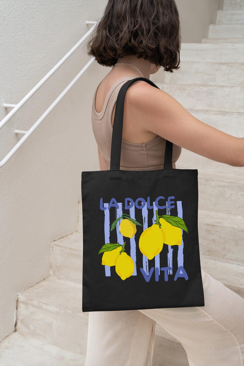 A woman is walking down a staircase while carrying a black tote bag with a graphic design featuring lemons and the text "LA DOLCE VITA".