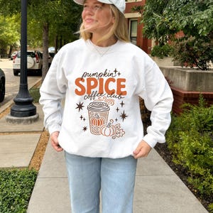 White sweatshirt with "pumpkin spice coffee club" text and fall graphic.