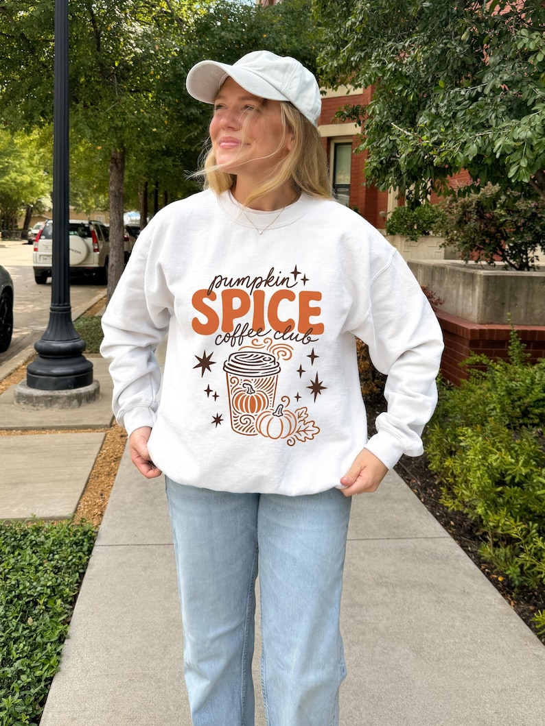 White sweatshirt with "pumpkin spice coffee club" text and fall graphic.