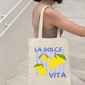 A woman is walking down a staircase while carrying a tote bag with a design featuring lemons and the text "LA Dolce Vita".