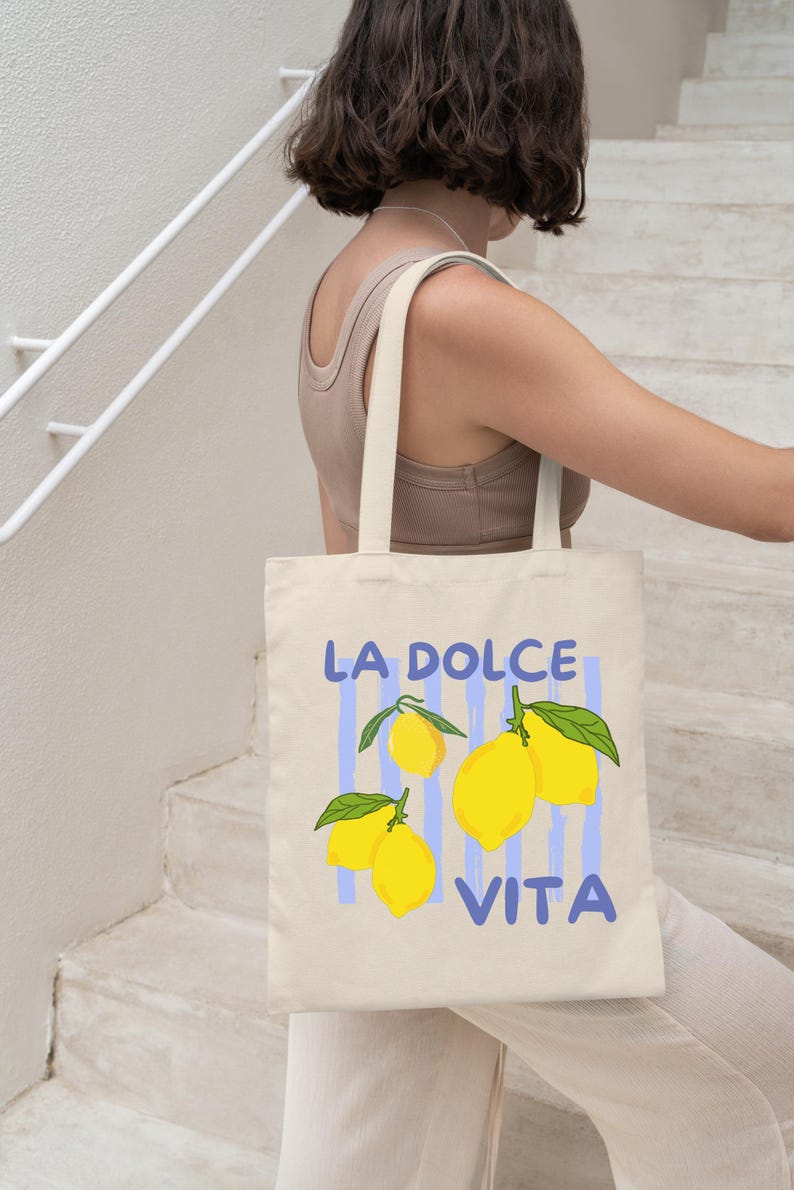 A woman is walking down a staircase while carrying a tote bag with a design featuring lemons and the text "LA Dolce Vita".