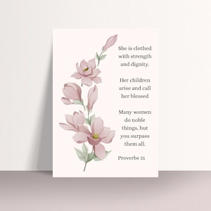 Puede incluir: Una impresión artística floral con una ilustración de acuarela de flores de magnolia rosas y hojas verdes. La impresión incluye el texto "She is clothed with strength and dignity" y una cita de Proverbios 31.