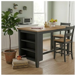 May include: A kitchen island with a natural wood top and a dark gray base featuring three open shelves, accompanied by two matching chairs with wood seats. A stack of three books and a copper measuring cup sit on the floor near a potted plant.