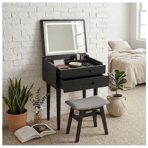 May include: A black vanity table with a flip-top mirror featuring integrated LED lighting, two storage drawers, and a matching stool with a gray upholstered seat. The vanity has four tapered legs and an open compartment for cosmetics.