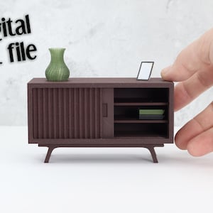 May include: A miniature brown cabinet with a sliding door, shelves, and angled legs. A green vase and a small framed picture sit on top. The text "Digital STL file" is in the upper left corner. The cabinet is approximately 4 inches wide.