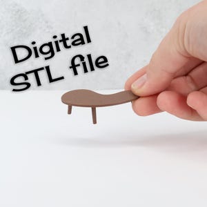 Könnte beinhalten: Ein kleiner, brauner Miniaturtisch mit drei Beinen wird in einer Hand gehalten. Der Tisch hat eine geschwungene Oberseite. Der Text im Bild lautet "Digital STL file". Der Hintergrund ist hellgrau.