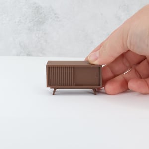 May include: A miniature brown wooden cabinet with a sliding door and four legs. The cabinet is about 6 inches long.