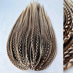 Puede incluir: Colección de extensiones de cabello trenzado en varios tonos de marrón, beige y negro. Las trenzas están tejidas apretadamente y dispuestas en forma de abanico, con una vista de cerca de los detalles de la trenza en el lado derecho. Extensiones para añadir longitud y volumen.