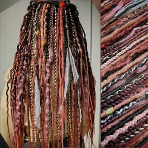 May include: A collection of handmade dreadlocks in shades of red, brown, and pink. The dreads are adorned with decorative elements like lace, beads, and wrapped threads. The style features a variety of textures and thicknesses, creating a unique and bohemian look.