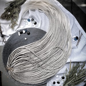 May include: A set of long, light-blonde synthetic hair extensions featuring numerous thin, uniform braids. The braids are arranged in a curved, flowing pattern, bundled together at one end with a simple brown string tie.