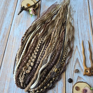 Puede incluir: Un conjunto de rastas sintéticas en tonos marrón, beige y crema, con diversas texturas que incluyen mechones trenzados, cordones retorcidos y cabello ondulado suelto. La colección incluye elementos decorativos como encaje, cuentas y dijes.