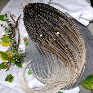 May include: A set of synthetic hair extensions featuring dark brown braided roots that transition into light blonde, straight ends. The braids are adorned with small, round wooden and metallic beads in shades of brown, gold, and cream, tied with twine.