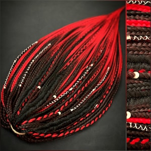 Puede incluir: Un conjunto de rastas sintéticas rojas y negras. Las rastas están dispuestas en forma de lágrima, con el color rojo dominando la parte superior y pasando al negro. Cuentas y costuras blancas acentúan las trenzas.