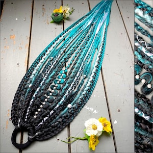 May include: A set of teal, black, and white synthetic dreadlocks, decorated with beads and white ribbon. The dreadlocks are fanned out, with a black hair tie at the base. The image also includes a few small flowers.