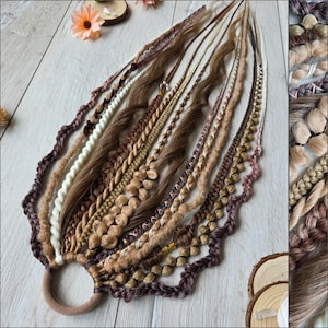 Könnte beinhalten: Eine Sammlung brauner, beiger und weißer Haarverlängerungen, darunter Zöpfe, Drehungen und Dreadlocks, die an einem braunen Haargummi befestigt sind. Die Extensions variieren in Textur und Stil, einige weisen dekorative Elemente auf. Die Anordnung wird auf einer hellen Holzoberfläche präsentiert.