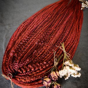 May include: A bundle of reddish-brown synthetic hair braids. The braids are tightly woven, with a textured appearance. Dried flowers and twine are included, adding a decorative element. The braids are likely for hair extensions or styling, a popular hair accessory.
