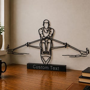 May include: A black metal wire sculpture depicting a person rowing a boat, mounted on a rectangular base with the words Custom Text printed on the front. The sculpture features a stylized figure holding two oars extending outward to the sides.