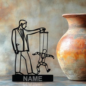 May include: A black metal sculpture depicts a person controlling a puppet, with the word "NAME" on the base. A large, textured, orange and brown ceramic vase with a handle is to the right.