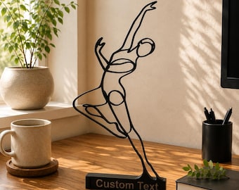 May include: A black metal wire sculpture depicting a dancer in a dynamic pose, mounted on a rectangular base with the words Custom Text printed on the front. The sculpture features continuous lines forming the silhouette of a figure in motion.