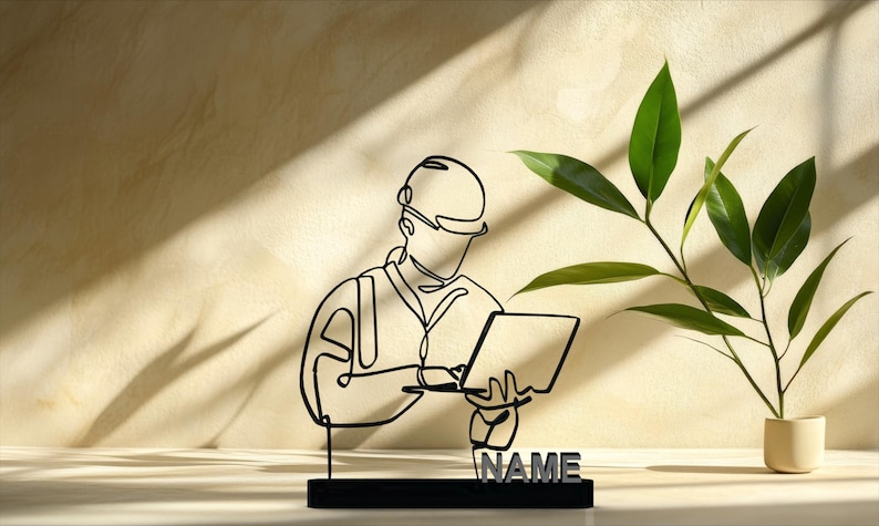 Puede incluir: Escultura de metal negro de un trabajador de la construcci&oacute;n sosteniendo una tableta, con la palabra "NAME" en la base. Una planta verde en una peque&ntilde;a maceta beige est&aacute; a la derecha. La escultura es de estilo dibujo lineal.