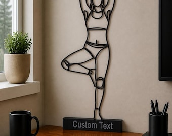 Peut inclure: Une décoration murale en fil de fer noir représentant une personne dans la posture de l'arbre de yoga. La silhouette repose sur une base rectangulaire noire portant l'inscription Custom Text en police sans empattement.