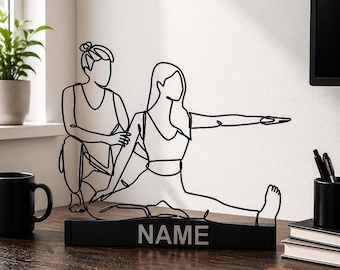 Peut inclure: Une sculpture en fil de fer noir représentant deux silhouettes en postures de yoga, l'une à genoux et l'autre assise avec une jambe tendue. La sculpture est fixée sur une base rectangulaire noire avec le mot NAME écrit en lettres capitales blanches.