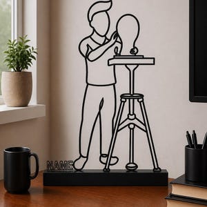May include: A black metal wire art sculpture depicting a person standing at a tripod stand working on a head-shaped form. The sculpture is mounted on a rectangular black base with the word NAME integrated into the design on the left side.