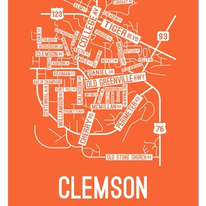 May include: A white line art map of Clemson, South Carolina, with the city name in large white letters at the bottom. The map shows the major roads and streets in the city, including Tiger Blvd, Old Greenville Hwy, and College Ave. The map is on an orange background.
