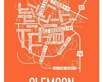 May include: A white line art map of Clemson, South Carolina, with the city name in large white letters at the bottom. The map shows the major roads and streets in the city, including Tiger Blvd, Old Greenville Hwy, and College Ave. The map is on an orange background.