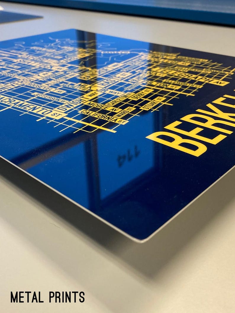 May include: A blue metal print with a yellow map of Berkeley, California. The map includes street names and landmarks. The text "BERKELEY" is printed in large yellow letters at the bottom right corner.