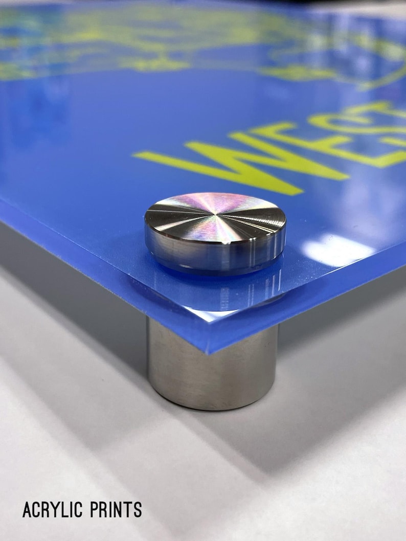 May include: Close-up of a blue acrylic print with a yellow inscription. The print is mounted on a clear acrylic stand with a silver metal base.