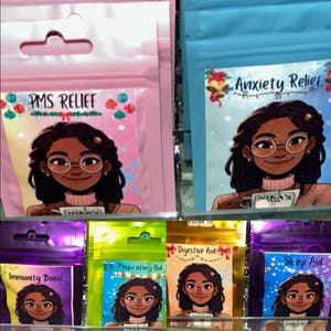 May include: A collection of small, colorful pouches with illustrations of a woman with long dark hair and glasses. Each pouch has a different label, including "PMS Relief", "Anxiety Relief", "Digestive Aid", "Sleep Aid", "Respiratory Aid", and "Immunity Boost".