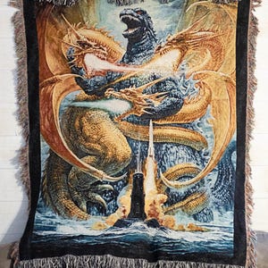 May include: A woven tapestry featuring a blue Godzilla-like monster with three golden dragons surrounding it. The monster is standing on a submarine with smoke and fire coming from the top. The background is a blue ocean with white waves.