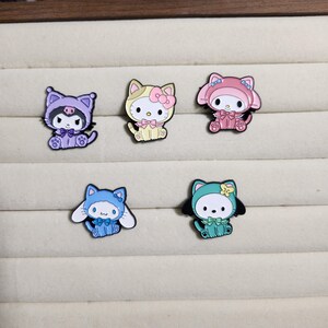 May include: Five enamel pins featuring different cartoon characters dressed in various costumes. The characters are all wearing hats and have different colored eyes and facial expressions. The pins are all in different colors, including pink, blue, green, yellow, and purple.