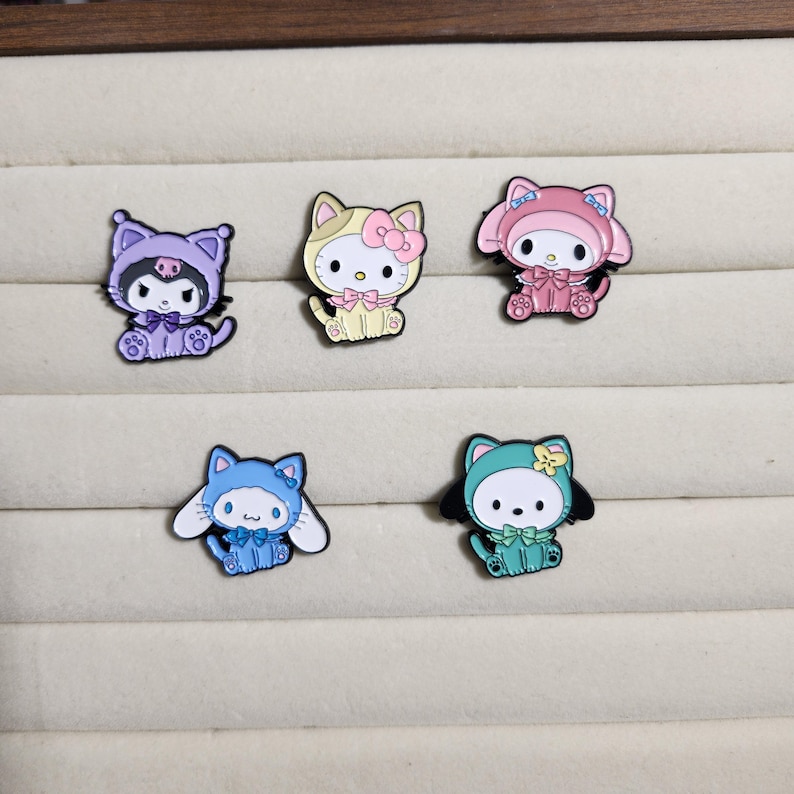 May include: Five enamel pins featuring different cartoon characters dressed in various costumes. The characters are all wearing hats and have different colored eyes and facial expressions. The pins are all in different colors, including pink, blue, green, yellow, and purple.