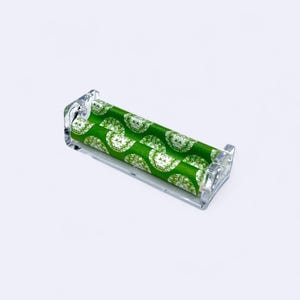 May include: A clear plastic rolling machine with a green and white patterned paper insert. The paper has a repeating pattern of white circles on a green background.