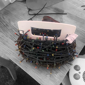 May include: A tangled string of black Christmas lights with multi-coloured bulbs. The lights are wrapped around a white plastic spool. The text on the spool reads "International Ltd. The Home of Christmas Trees"