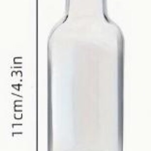May include: A transparent glass bottle with a narrow neck and a rounded body. The bottle is 11cm tall and 3.2cm wide. The bottle has a 50ml capacity. The bottle is empty and ready to be filled.