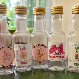 May include: Five clear mini spirit bottles with gold lids, each with a different label. The labels feature text and graphics for a hen party, including phrases like "Sophie's Hen Do" and "Emily's Hen".