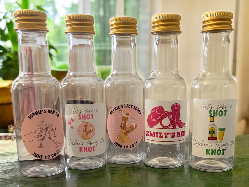 May include: Five clear mini spirit bottles with gold lids, each with a different label. The labels feature text and graphics for a hen party, including phrases like "Sophie's Hen Do" and "Emily's Hen".
