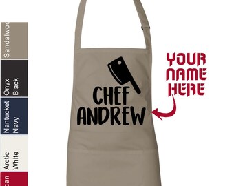 May include: A tan chef's apron with a black chef's knife graphic and the text "Chef Andrew". The apron has a large pocket on the front. The text "Your Name Here" is written in red on the right side of the apron.