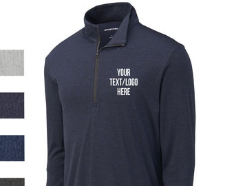 May include: Navy blue long-sleeve quarter-zip pullover with the text "YOUR TEXT/LOGO HERE" in white. The shirt has a mock neck collar and a black zipper. The fabric has a textured appearance.